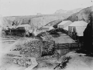 A view of Treffry fish cellar, above Towan Beach, with the buildings and cliff behind. Treffry was built around 1845 and was located in the middle of Towan Promenade. It was also known as the 'Flour and Fat' although it is not known where the  cellar got this nickname from. The cellar's huer was William Osborne, the master seiner was Isaac Pappin and the agent was Thomas Jenkin. Photographer: Unknown.